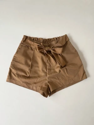 Beiga shorts med knyt i midjan - Snygga beiga shorts med hög midja och knytband i midjan. Aldrig använda 🤍 söta till sommaren med toppar 