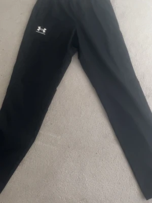Svarta mjukisbyxor från Under Armour storlek S helt nya - Svarta mjukisbyxor från Under Armour med elastisk midja och diskret logga på låret. Tillverkade i ett lätt och ventilerande material med meshfoder, perfekta för chill eller träning. Snygg och enkel design som funkar till det mesta.