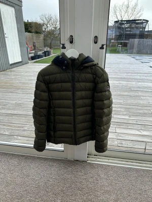 Mörkgrön pufferjacka med huva - Snygg mörkgrön volmar jacka. Lätt quiltad och bra till hösten/våren. Nästintill helt ny. Ett litet hål i armen