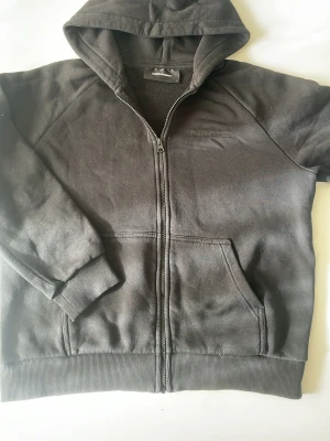 Svart hoodie från Peak Performance - Svart hoodie med dragkedja från Peak Performance. Klassisk modell med broderad logga på bröstet, två fickor fram och ribbade muddar. Mjuk bomullsblandning och huva med dragsko. Perfekt för en avslappnad och sportig stil. Pris kan diskuteras!!!!