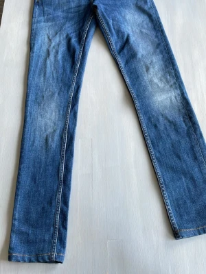 Blå raka jeans med klassisk tvätt från Tiger of sweden - Säljer ett par blå jeans med rak passform och klassisk tvätt. Jeansen har fem fickor, gylf med dragkedja och knapp samt kontrastsömmar. Perfekta för en avslappnad stil och funkar året runt.