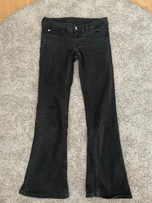 Svarta bootcut jeans från Cheap Monday - Snygga svarta bootcut jeans från Cheap Monday med klassisk femficksdesign och ikonisk logga i rosa på bakfickan. Jeansen har utsvängda ben och låg midja, perfekta för en trendig och avslappnad stil.