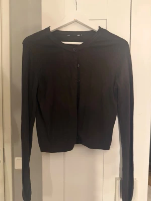 Brun kofta från 157, storlek M - Mysig brun kofta från 157 med rund halsringning och knäppning framtill. Långärmad modell i mjukt stickat material, perfekt att slänga över en t-shirt eller linne. Enkel och stilren design som passar till det mesta.