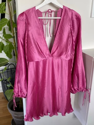Satinveckad vacker miniklänning i cerise till student/examen!  - Cerise plisserad miniklänning i satin med djup urringning och blusärmar med knytning nedtill.  Klänningen är fodrad. (Se bilder, lite ljusare rosa färg på fodret) Dragkedja bak med ett litet knäppe.   Denna vackra festklänning är endast använd vid 1 tillfälle, så absolut nyskick!  Material 100 % polyester  Skötselråd Maskintvätt kallt  Silkeslen klänning  Nypris 798kr  Nu är den slutsåld så passa på! 💕 Mått finns i bilderna  