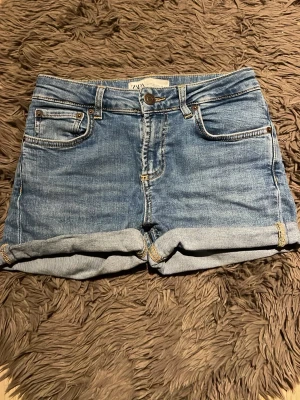 Blå jeansshorts från ZARA - Snygga blå jeansshorts från ZARA med klassisk femficksdesign och uppvikta benslut. Perfekta för varma dagar och enkla att matcha med olika toppar. 