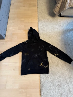 Svart Jordan hoodie med guldtryck, storlek L 12-13år  - Säljer en svart hoodie från Jordan med huva och guldiga detaljer, jag har bara använt den 1 gång.