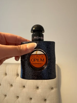 YSL Black Opium Eau de Parfum 30ml - YSL Black Opium Eau de Parfum i en snygg svart glittrig flaska med rund orange detalj och svart kork. Flaskan rymmer 30 ml och har en modern, lyxig design som sticker ut på parfymhyllan. Perfekt för dig som gillar ikoniska dofter och stilren look. Ungefärlig mängd som finns kvar i flaskan syns på bild