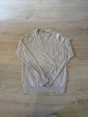 Beige stickad tröja med rund hals - Snygg beige stickad tröja med rund halsringning och långa ärmar. Tröjan har ribbstickade muddar vid ärmslut och nederkant, vilket ger en stilren look. Perfekt för lager-på-lager och enkel att matcha med olika outfits.