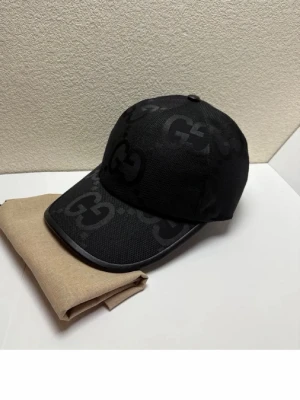 Svart keps med GG-mönster - Snygg svart keps med det klassiska GG-monogrammet i ton-i-ton. Kepsen har böjd skärm och är tillverkad i ett slitstarkt tygmaterial. Perfekt accessoar för att lyfta din streetwear-look.