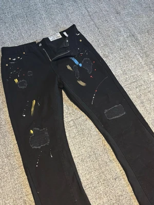 Svarta jeans med färgstänk och slitningar - Unika svarta jeans med coola färgstänk i blått, gult och rött samt trendiga slitningar och patchade detaljer🤩. Raka ben och klassisk femficksmodell. Perfekta för dig som gillar streetstyle och vill sticka ut med din outfit✨. För mer bilder och diskussioner om priser kom dm😝