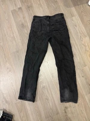 Svarta jeans från Jack & Jones - Säljer ett par svarta jeans från Jack & Jones med raka ben och klassiska bakfickor. Jeansen har en diskret tvättad look och är tillverkade i bomull. Perfekta för en avslappnad stil.