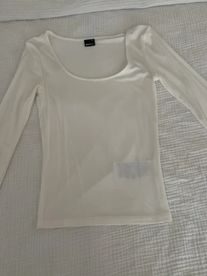 Vit långärmad topp från Gina Tricot - Snygg vit långärmad topp från Gina Tricot med rundad urringning. Tunn och stretchig i materialet, perfekt att styla med jeans eller kjol. Enkel och stilren design som passar till många olika looks.