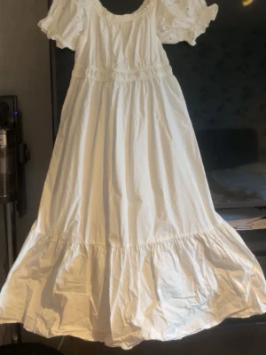 Vit långklänning - Vit lång klänning med bred volangkant nertill och puffiga kortärmar med broderade detaljer. Klänningen har resår i midjan och en rundad halsringning som man kan styla på alla möjliga sätt. Perfekt för sommarens alla tillfällen!