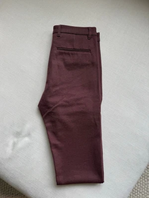 Lila  kostymbyxor i slim fit - Snygga lila kostymbyxor med slim passform och klassiska bakfickor. Byxorna har bälteshällor och är tillverkade i ett mjukt material som ger en dressad look. Perfekta för dig som gillar stilrena och moderna byxor.