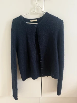 Mörkblå kofta från Gina Tricot - Mysig mörkblå kofta från Filippa K med rund halsringning och knäppning framtill. Koftan har lång ärm och är tillverkad i ett fluffigt, mjukt material som ger en avslappnad look. Perfekt att slänga över en t-shirt eller topp.