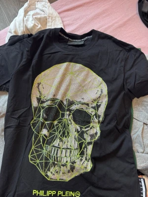 Svart Philipp Plein t-shirt med dödskalle - Cool svart t-shirt från Philipp Plein med stort dödskalletryck i silver och neongult framtill. Passar s/m