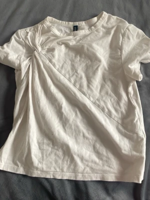 Vit t-shirt med twistad detalj - Snygg vit t-shirt från H&M med unik twistad detalj vid axeln som ger en cool draperad effekt. T-shirten har rund halsringning och korta ärmar, perfekt för en avslappnad och trendig look.