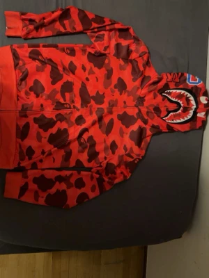 Röd BAPE Shark Hoodie - Säljer en Röd BAPE hoodie som är full zip hela vägen upp. Den är bra material och perfekt inför sommaren, Nytt skick och liknar en haj.