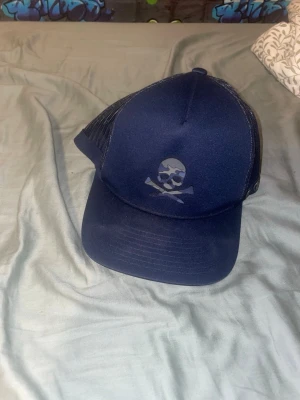 Marinblå keps från G/FORE - Snygg marinblå keps från G/FORE med mesh på sidorna och justerbar snapback. Framtill finns en cool dödskalle med korslagda klubbor. Perfekt för dig som vill sticka ut med en sportig och trendig look.