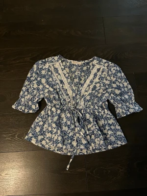 Blommig blåvit blus med spetsdetaljer - Sååå fin blus! Den har ett knyte i midjan så man bestämmer själv hur löst/hårt man knyter. Passar även en M💕
