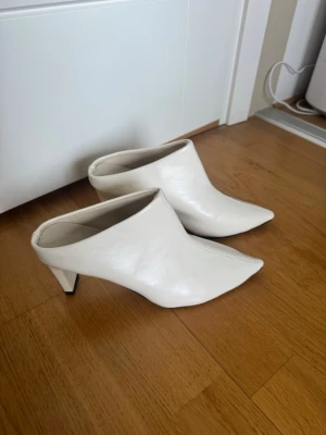 Vita spetsiga mules med klack - Snygga vita pumps i mule-modell med spetsig tå och markerad klack. Skorna har en stilren design i slätt material och öppen häl, vilket ger en modern och trendig look. Perfekta för dig som gillar minimalistisk stil och vill sticka ut. Slip in klackskor ❤️