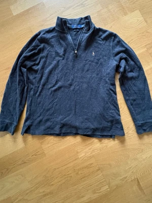  half zip tröja Polo Ralph Lauren - Mörkgrå långärmad tröja från Polo Ralph Lauren med klassisk broderad logga på bröstet. Tröjan har en half zip-dragkedja vid kragen och är tillverkad i ett mjukt material som passar perfekt till vardags.