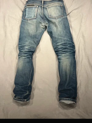 Blå slitna jeans med raka ben - Säljer ett par blå jeans med snyggt slitna detaljer och raka ben. Jeansen har klassiska bakfickor och kontrastsömmar. Perfekta för en avslappnad och trendig look. Materialet är denim i bomull.