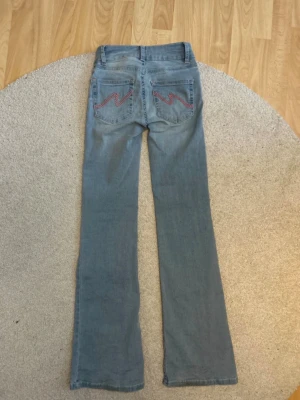 Ljusblå bootcut Nelly jeans  - Säljer ett par ljusblå bootcut jeans med snygg rosa brodyr på bakfickorna. Jeansen har klassisk femficksmodell och låg midja. Är lite smutsiga vid hälen men det är inget som man tänker på när man har de på sig💗Nypris 799💗Buda gärna!💗