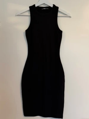 Svart tight ärmlös klänning  - En svart, tight och ärmlös klänning med rund halsringning. Klänningen har en kroppsnära passform och är i en enkel, stilren design som passar perfekt till många olika tillfällen 🩷