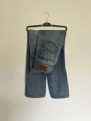 Blå raka jeans från Mavi  - Snygga blå jeans från Mavi med klassisk femficksdesign och raka ben. Jeansen har en ljus tvätt och subtila slitningar framtill för en avslappnad look. Tillverkade i bomull med Mavi logga på bakfickan. Storlek 33/32