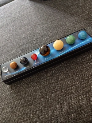 Solsystemet planetmodell i glas - Snygg planetmodell av solsystemet med åtta glaskulor som representerar planeterna. Varje planet har sin egen färg och placeras i en svart rektangulär låda med namn under varje kula. Perfekt som dekoration eller present till rymdintresserade.