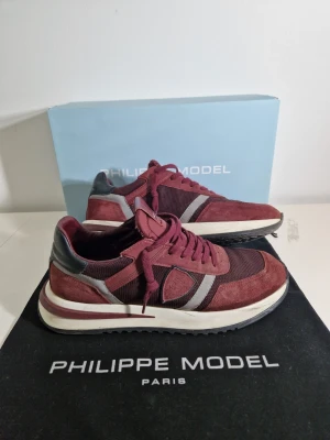 Philippe Model sneakers - Snygga sneakers från Philippe Model i vinrött mocka och mesh med grå och svarta detaljer. Skorna har vita och vinröda sulor samt klassisk låg siluett. Perfekta för dig som vill ha en stilren och trendig look. Går att förhandla priset