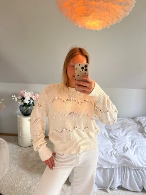 Vit stickad tröja med hålmönster - Snygg vit stickad tröja med vågigt hålmönster och ribbade muddar. Tröjan har en avslappnad passform och rund halsringning. Perfekt att matcha med jeans eller kjol för en trendig look.