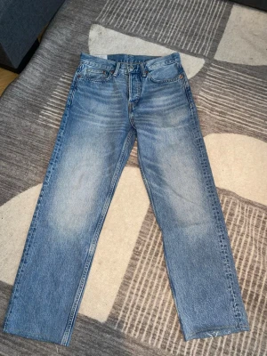 H&M Jeans 29/32 - Säljer ett par blå jeans med rak passform och klassisk femficksdesign. Jeansen har en ljus tvätt med snygga slitningar och normal midja. Perfekta för en avslappnad och trendig stil.