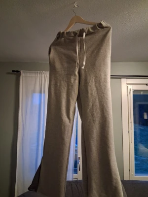 Grå vida mjukisbyxor med dragsko - Säljer ett par grå mjukisbyxor med vida ben och dragsko i midjan. Byxorna är tillverkade i mjukt sweatshirtmaterial och har en avslappnad passform. Perfekta för en chill och bekväm stil.
