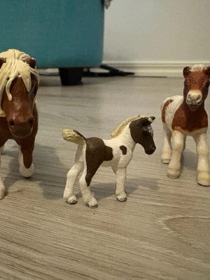 Små hästfigurer i plast - Tre realistiska hästfigurer i plast, målade i brunt och vitt. En av figurerna är mindre och passar perfekt som föl. Figurerna har fina detaljer och är perfekta för samling eller lek.