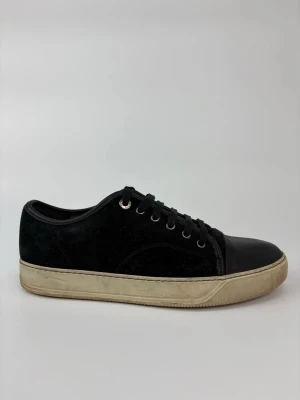 Svarta Lanvin sneakers med mocka och läder - Stilrena svarta sneakers med ovandel i mocka och tåparti i läder. Skorna har svarta snören, metallöljetter och en beige sula med retrovibbar. Perfekta för dig som gillar en clean och klassisk look.
