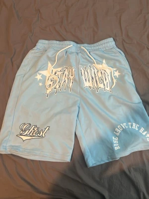 Blå shorts från Ghtst med tryck och Ralph lauren t sort - Blå shorts från Ghtst med vita tryck som 'STAY WILD' och 'RISE ABOVE THE HATE'. Shortsen har snörning i midjan och är perfekta för en avslappnad stil. Mjukt material och elastisk midja för extra komfort. Även polo t shirt 