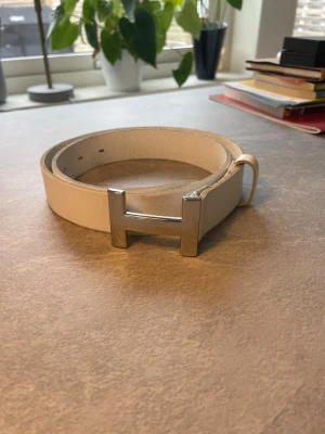 Vitt H-Bälte 100cm - Vitt läder bälte med ett silver spänne som ser ut som ett H.