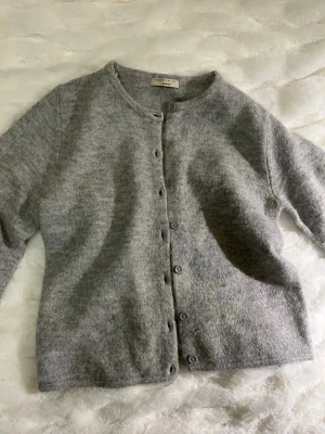 Grå kofta från Gina Tricot - Mysig grå kofta från Gina Tricot. Klassisk rak modell med rund halsringning och knäppning framtill. Perfekt att slänga på sig över en t-shirt eller skjorta. Enkel och stilren design som funkar till det mesta.