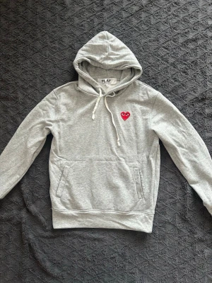 Grå hoodie från Comme des Garçons Play - Grå hoodie från märket comme des garçons play. Den är i storlek S och är endast använd få tal gånger skick: 9,2/10✅. Modellen på bilden är 183 och väger 72 kg. Hör av dig om du har några frågor