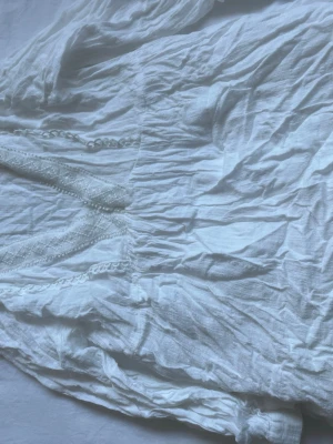 Vit klänning med spetsdetaljer från Zara - Säljer en luftig vit klänning från Zara med fina spetsdetaljer och lätt rynkad struktur. Klänningen har en romantisk känsla och är tillverkad i ett tunt, mjukt tyg som känns skönt mot huden.