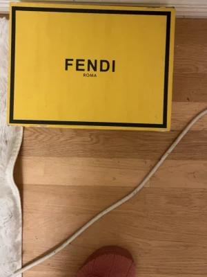 Fendi brun monogram axelväska - Säljer en brun axelväska från Fendi med klassiskt FF-monogram i svart. Väskan har guldfärgade metalldetaljer och dragkedja upptill. Snygg bågformad design och bred axelrem med samma mönster. Perfekt för dig som gillar lyxiga accessoarer.