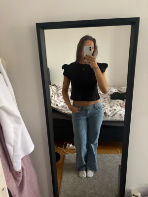 Svart croppad topp med volangärm - En svart croppad topp med volangärmar och rund halsringning. Toppen har en slim passform och är perfekt för dig som gillar en stilren men ändå trendig look. Materialet känns mjukt och lätt mot huden.