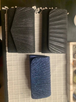 Tre glittriga kuvertväskor i svart och blått - Säljer tre kuvertväskor, två i svart och en i mörkblå. Väskorna har glittriga detaljer och elegant veckad design på framsidan. Väskorna är från shein och skickas med gratis vid köp av klänningarna. Annars 100kr för alla 3.