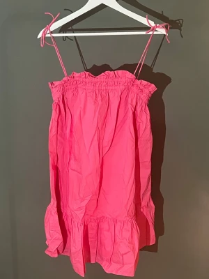 Rosa volangklänning med smala axelband - Supersöt rosa klänning med smala axelband som knyts upptill. Klänningen har volangdetaljer vid fållen och upptill, samt en avslappnad passform. Perfekt för varma dagar och ger en lekfull vibe🩷