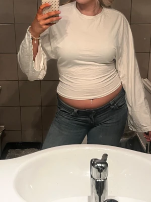 Vit långärmad topp med vida ärmar - Säljer en vit långärmad topp med snygga vida ärmar och rund halsringning. Toppen är figurnära och har en croppad passform som visar midjan. Perfekt att styla med jeans eller kjol för en trendig look.