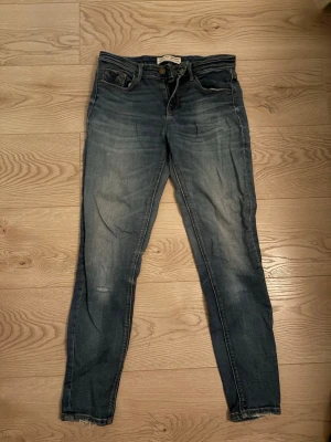Blå slim fit jeans från strandivarius - Snygga blå slim fit jeans från strandivarius med klassisk femficksdesign och slitna detaljer. Jeansen har en något tvättad look med ljusare partier på låren och knäna. Tillverkade i bomull med en bekväm passform och normal midja.