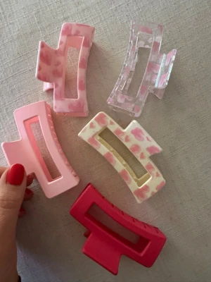 Set med fem hårklämmor i pastell - Säljer ett set med fem rektangulära hårklämmor i olika pastellfärger och mönster. Klämmorna är i rosa, rött, vitt och transparent med hjärtmönster. Tillverkade i plast och perfekta för att skapa snygga frisyrer.