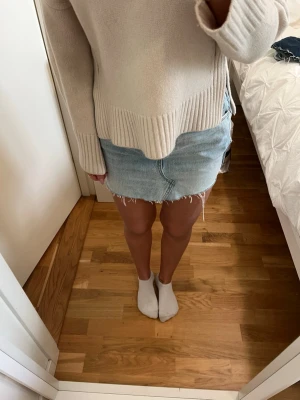 Ljusblå jeanskjol med fransig kant - Trendig ljusblå jeanskjol med rå, fransig nederkant och klassisk femficksdesign. Kjolen har en kort passform och är perfekt för en avslappnad och cool stil. Passar till både stickade tröjor och t-shirts.